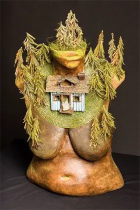 A painted plaster cast of a woman’s upper body with miniature cottage and trees.